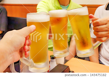在居酒屋（日本酒吧）裡，一隻手傾斜著啤酒杯，舉杯碰杯。 143475182