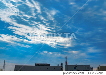 美麗的捲雲圖案在藍天的背景下,鋪展在建築物上方。 美麗的捲雲圖案在藍天的背景下,鋪展在建築物上方。 143475204