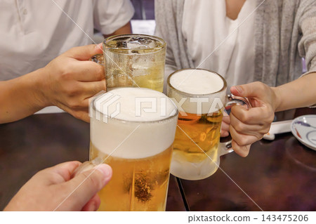 在居酒屋（日本酒吧）裡，一隻手傾斜著啤酒杯，舉杯碰杯。 143475206