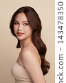 A beautiful young Asian woman with clean, fresh skin against a beige background. Skincare, facial treatment, cosmetology, beauty, and spa. An elegant portrait of an Asian woman. 143478350
