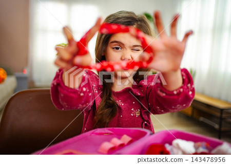 Little Girl Playing with Red Ribbon and Winking at Home Little Girl Playing with Red Ribbon and Winking at Home 143478956