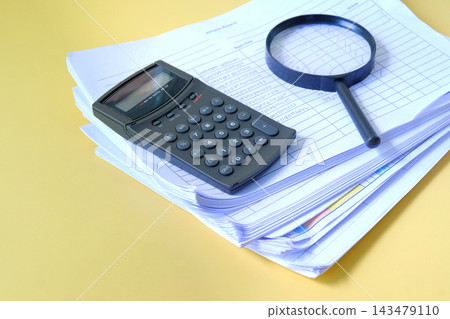 Magnifying glass and calculator on Stack of documents. 143479110