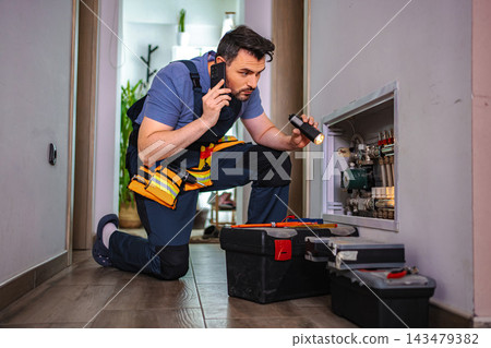 Plumber inspecting heating system while talking on smartphone Plumber inspecting heating system while talking on smartphone 143479382