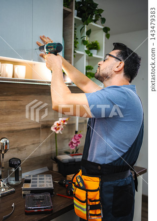 Man installing kitchen cabinet using cordless drill Man installing kitchen cabinet using cordless drill 143479383