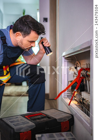 Handyman inspecting home plumbing system with flashlight Handyman inspecting home plumbing system with flashlight 143479384