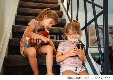 Children sisters sitting stairs watching smartphone screen time Children sisters sitting stairs watching smartphone screen time 143479387