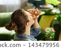 Woman Relaxing with Pizza Snack in Sunlit Home 143479956