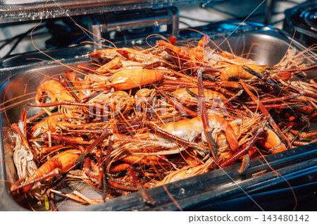 Large pile of cooked orange giant river prawns with long claws in stainless steel serving tray, seafood buffet presentation Large pile of cooked orange giant river prawns with long claws in stainless steel serving tray, seafood buffet presentation 143480142