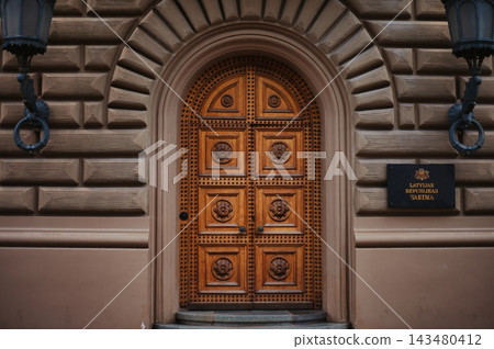 Symmetrical eye-level shot of a grand arched wooden door with intricate floral carvings and metal. Symmetrical eye-level shot of a grand arched wooden door with intricate floral carvings and metal. 143480412