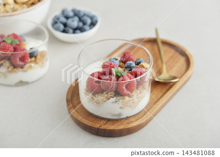 Yogurt dessert with granola and fresh raspberries and blueberries in a glass, served with a spoon 143481088