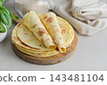 Stack of lavash or chapati flatbreads on a wooden cutting board, with a jar of flour, fresh basil 143481104