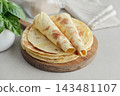 Stack of lavash or chapati flatbreads on a wooden cutting board, with a jar of flour, fresh basil 143481107
