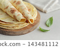 Stack of lavash or chapati flatbreads on a wooden cutting board, with a jar of flour, fresh basil 143481112
