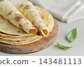 Stack of lavash or chapati flatbreads on a wooden cutting board, with a jar of flour, fresh basil 143481113