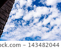 Brick building edge beneath a blue sky filled with white clouds. Cloudscape and architecture contrast. Weather and atmosphere concept. Open sky for design and copy space. 143482044