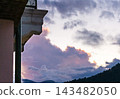 Cloudy sunset over mountain ridge beside building balcony. Dramatic sky and cloudscape. Evening weather and nature background. Mountain landscape at dusk with architectural foreground. 143482050