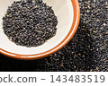 Roasted black sesame seeds served on a white plate, nutrient-rich black sesame seeds shining brightly on the dining table. 143483519
