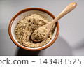 A mortar and pestle containing ground sesame seeds and a wooden spoon; a scene of preparation for cooking. 143483525