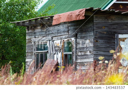 Dilapidated wooden shack with weathered dark timber planks and decaying window frames situated in a rural landscape, showcasing rustic textures and abandoned architecture in the countryside 143483537