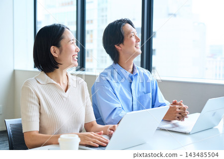 一對夫婦坐在明亮的窗邊座位上,微笑地討論著他們的新生活和財富累積。 一對夫婦坐在明亮的窗邊座位上,微笑地討論著他們的新生活和財富累積。 143485504