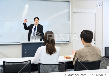 一位身穿西裝的男教師正在教室裡熱情地為學生講課。 一位身穿西裝的男教師正在教室裡熱情地為學生講課。 143485894