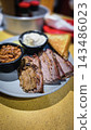 Smoked brisket served with baked beans, creamy mashed potatoes and toast on a casual barbecue plate. Hearty comfort-food meal showcasing tender meat, smoky flavors 143486023
