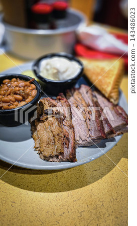 Smoked brisket served with baked beans, creamy mashed potatoes and toast on a casual barbecue plate. Hearty comfort-food meal showcasing tender meat, smoky flavors 143486023