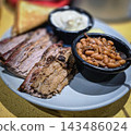 Smoked brisket served with baked beans, creamy mashed potatoes and toast on a casual barbecue plate. Hearty comfort-food meal showcasing tender meat, smoky flavors 143486024