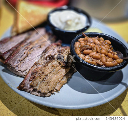 Smoked brisket served with baked beans, creamy mashed potatoes and toast on a casual barbecue plate. Hearty comfort-food meal showcasing tender meat, smoky flavors 143486024