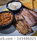 Smoked brisket served with baked beans, creamy mashed potatoes and toast on a casual barbecue plate. Hearty comfort-food meal showcasing tender meat, smoky flavors 143486025