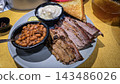 Smoked brisket served with baked beans, creamy mashed potatoes and toast on a casual barbecue plate. Hearty comfort-food meal showcasing tender meat, smoky flavors 143486026
