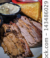 Smoked brisket served with baked beans, creamy mashed potatoes and toast on a casual barbecue plate. Hearty comfort-food meal showcasing tender meat, smoky flavors 143486029