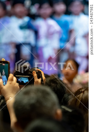 Parents recording their children school performance with camera, audience engagement at a school event Parents recording their children school performance with camera, audience engagement at a school event 143487981