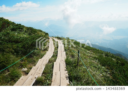 兩條木棧道沿著綠草茵的山脊延伸至夏日的天空。 兩條木棧道沿著綠草茵的山脊延伸至夏日的天空。 143488369