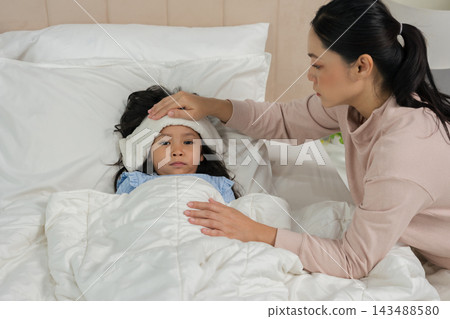 mother applying cold compress on sick daughter's forehead in bed mother applying cold compress on sick daughter's forehead in bed 143488580