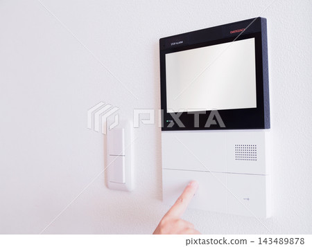 一隻手正在按下安裝在牆上的對講機(門鈴)上的開關。 一隻手正在按下安裝在牆上的對講機(門鈴)上的開關。 143489878