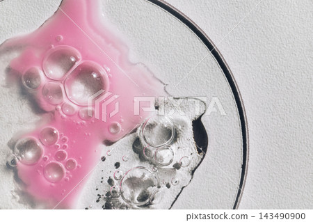 Pink and clear liquids mixing with bubbles on laboratory glass dish Pink and clear liquids mixing with bubbles on laboratory glass dish 143490900