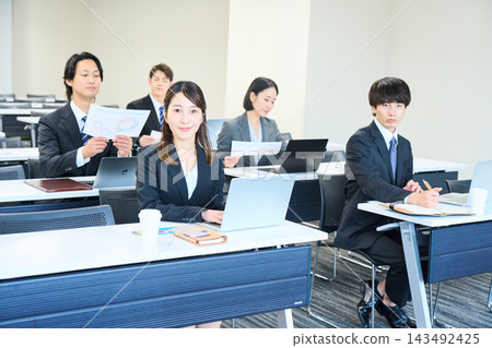 身穿西裝的男女,打開筆記型電腦,正在會議室接受訓練。 身穿西裝的男女,打開筆記型電腦,正在會議室接受訓練。 143492425