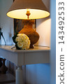 Wedding Bouquet of Cream Roses on a Console Table Beside a Warm Lit Lamp in a Cozy Home Interior 143492533