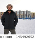 Front view of a happy smiling bearded man standing on snow outdoors wearing warm winter fur hat. 143492652