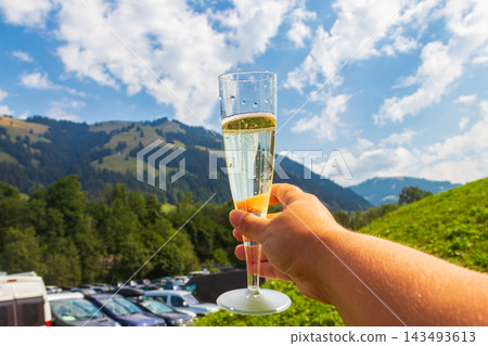 Hand holding a glass of sparkling champagne with a scenic alpine mountain landscape in Switzerland Hand holding a glass of sparkling champagne with a scenic alpine mountain landscape in Switzerland 143493613