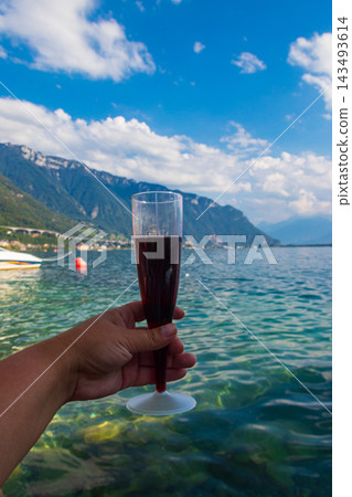 Hand holding a glass of red wine with a scenic panoramic view of Lake Geneva in Montreux, Switzerland 143493614