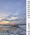 Setting sun glows above foamy ocean waves beneath layered evening clouds. 143493698