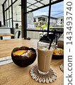 Iced coffee and mango-topped fruit bowl sit on a cafe table in natural daylight. 143493740