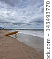 Yellow rescue board rests beside ocean surf on a sandy beach in overcast daylight. 143493770