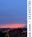 Pink sunset clouds glow above tiled neighborhood rooftops and illuminated windows at twilight. 143493780