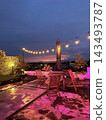 String lights illuminate wooden rooftop seating and potted plants beneath a colorful twilight sky 143493787