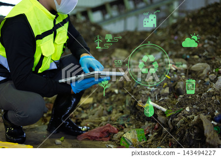 Asian engineer in hardhat using tablet with green energy and carbon neutral HUD graphics inside recycling factory 143494227