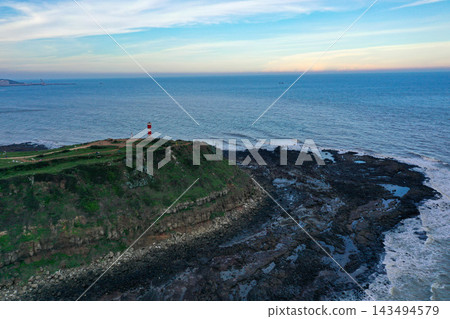 Aerial view of a green coastal cape in China with a lighthouse and calm sea. 143494579