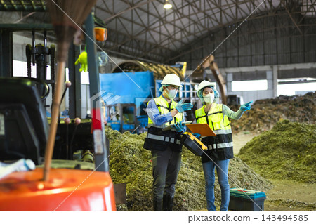 Two industrial engineers in safety vests and helmets collaborating and gesturing while inspecting waste sorting operations inside Two industrial engineers in safety vests and helmets collaborating and gesturing while inspecting waste sorting operations inside 143494585